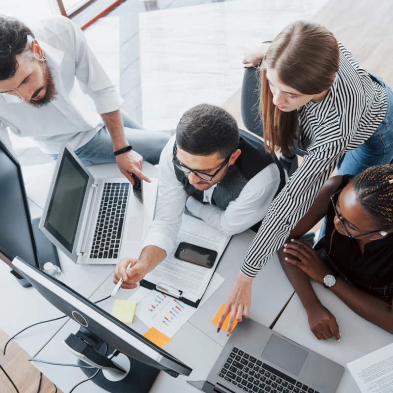 Découvrez RHSelect et notre approche du recrutement Vue de haut d'un groupe de quatre personnes réunies autour d'un ordinateur sur un même bureau.